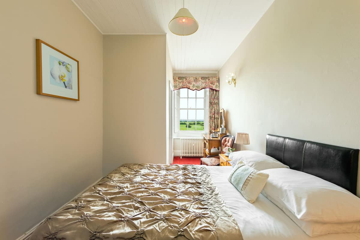 Une chambre avec un grand lit, un tableau encadré au mur et une fenêtre avec des rideaux.
