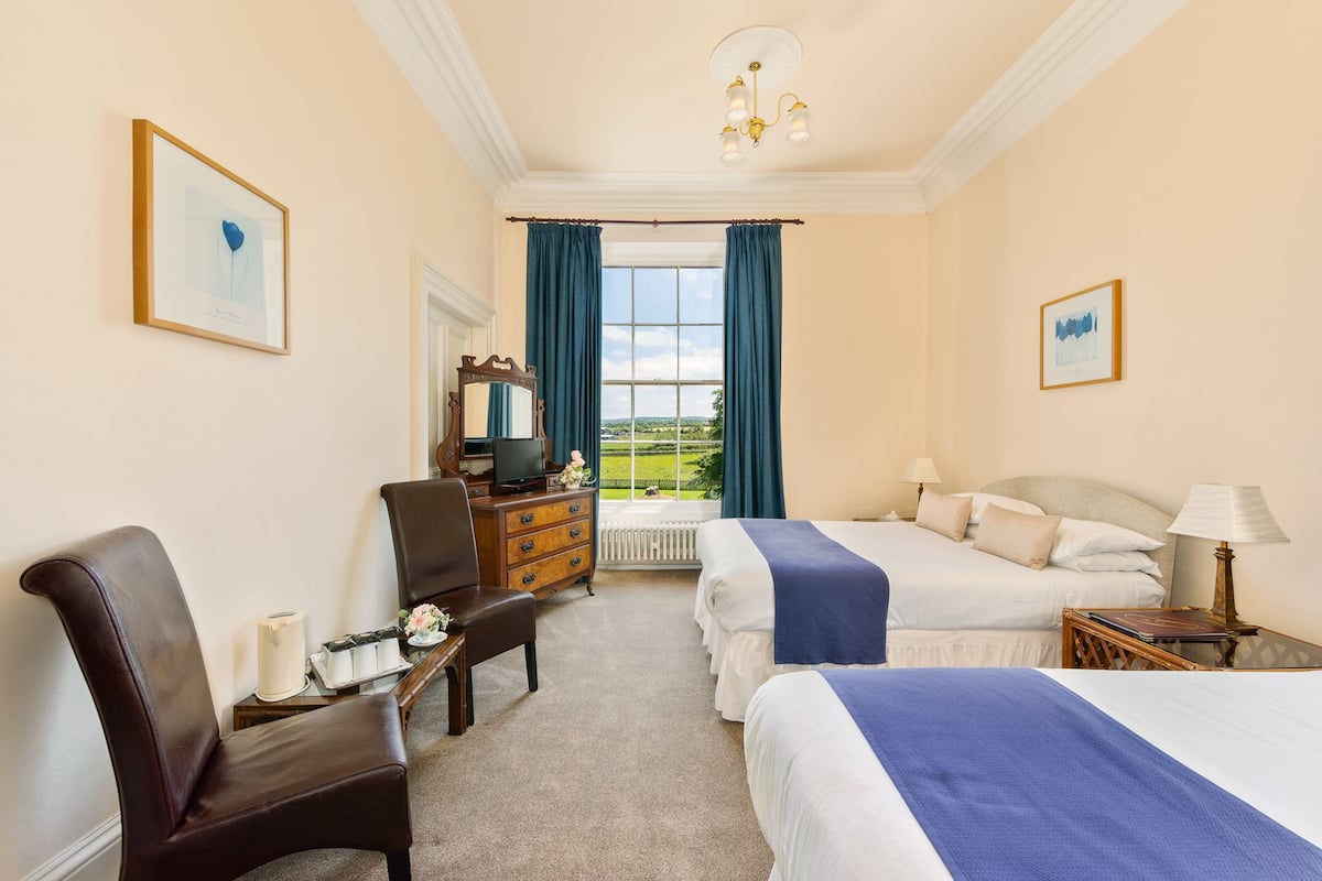 Une chambre d’hôtel avec deux lits, un bureau avec un ordinateur, une chaise et une vue sur l’extérieur.
