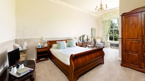 A bedroom with a wooden bed, bedside tables, a desk, a wardrobe, and a window with curtains. - Greenhill Hotel (Wigton)