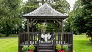 A gazebo with a table and chairs, surrounded by potted plants and a well-maintained lawn. - Greenhill Hotel (Wigton)