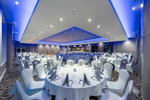 A banquet hall with round tables, white chairs, and a bar area. - Greenhill Hotel (Wigton)