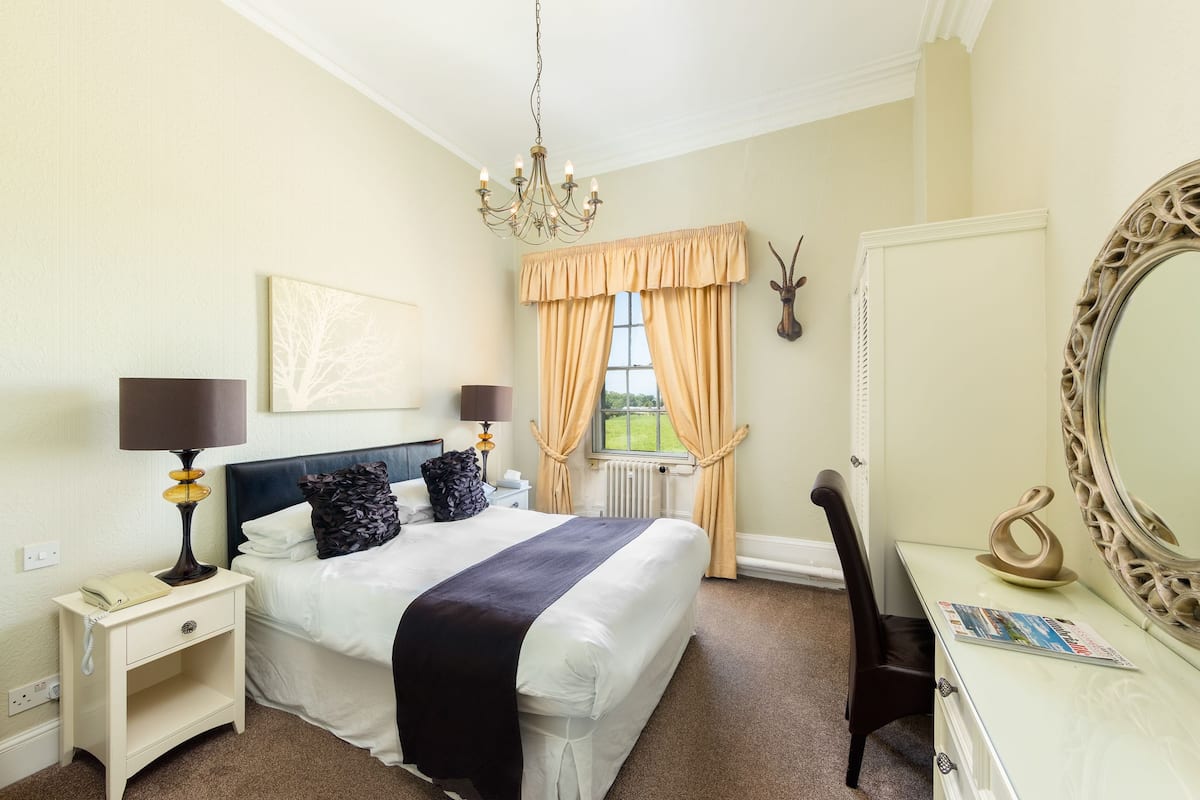 Une chambre à coucher bien rangée, avec un lit, des tables de chevet, une commode, un miroir et une fenêtre avec des rideaux.