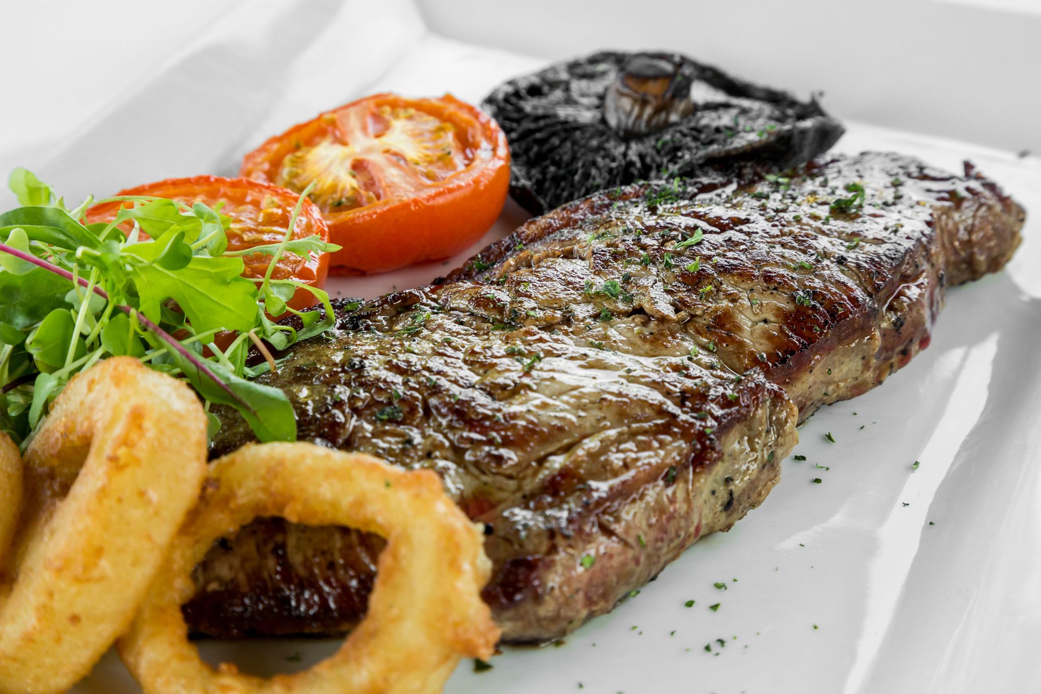 Bistec con verduras a la parrilla y aros de cebolla, sobre un plato blanco.