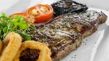 Bistec con verduras a la parrilla y aros de cebolla, sobre un plato blanco.