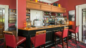 A bar area with a wooden counter, red bar stools, and shelves stocked with bottles. - Greenhill Hotel (Wigton)