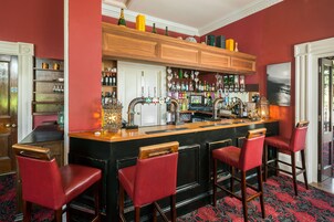 A bar area with a wooden counter, red bar stools, and shelves stocked with bottles.