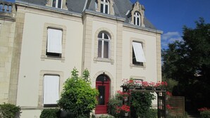 A large, historic building with a red door, multiple windows, and a garden with red flowers. - Beausejour Hotel (Chauvigny)