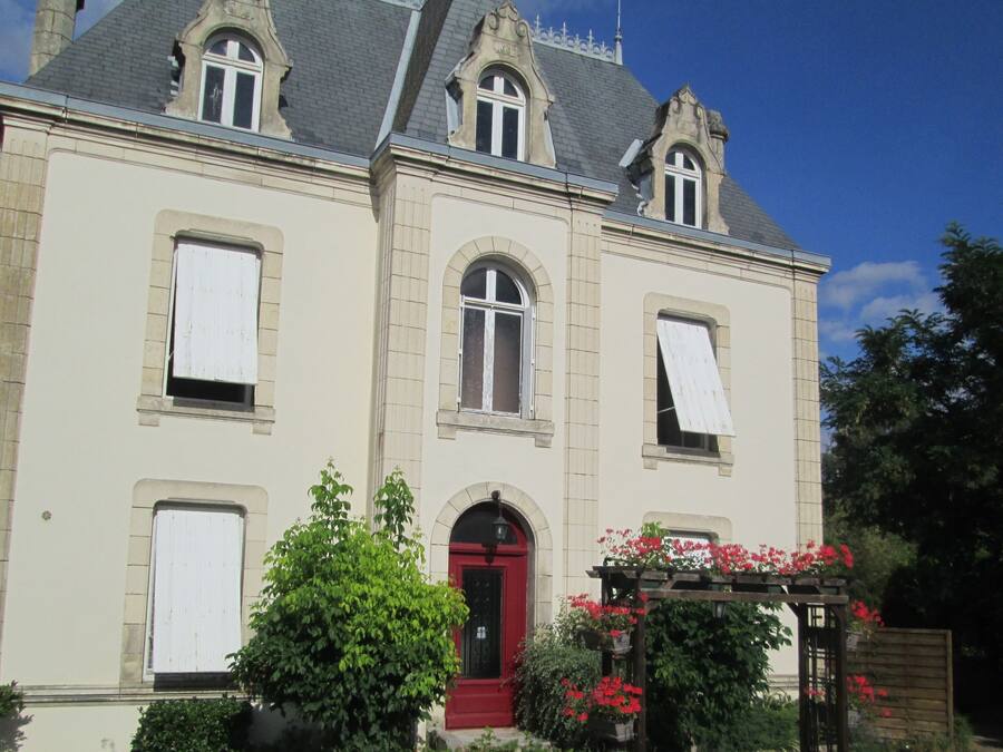 Ein großes, historisches Gebäude mit roter Tür, zahlreichen Fenstern und einem Garten mit roten Blumen.