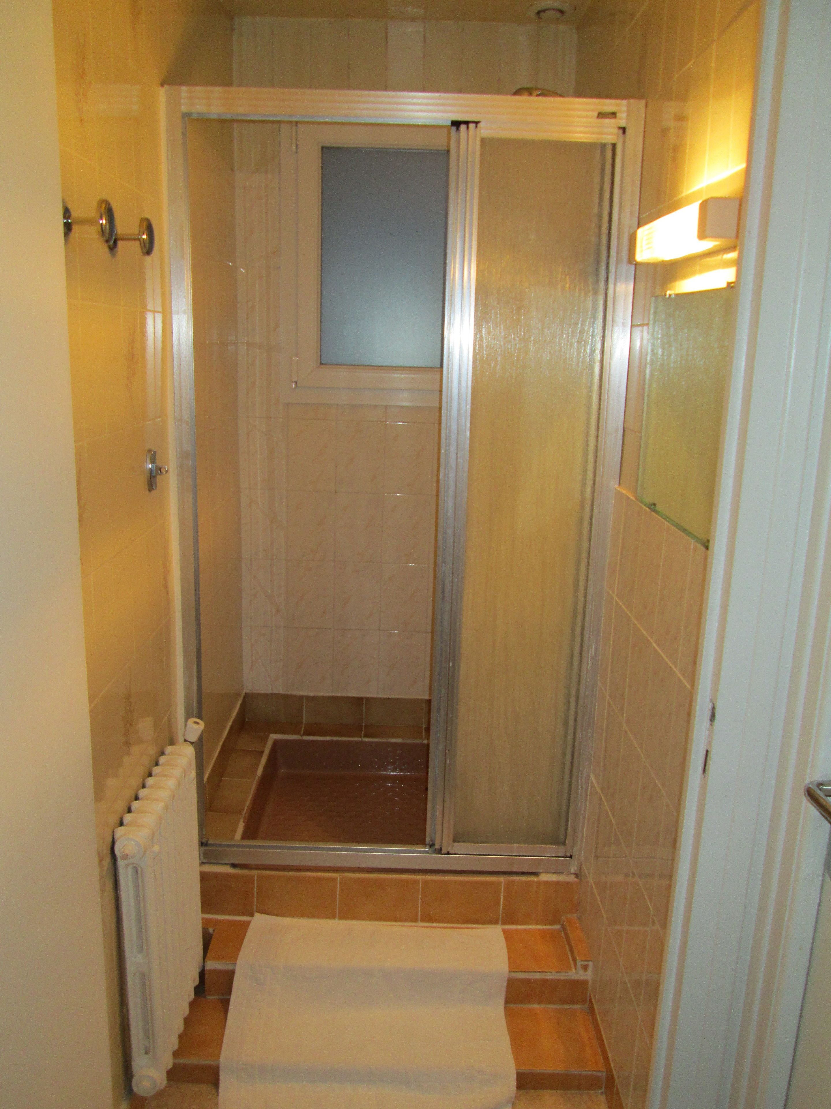 A small, enclosed shower area with a glass door, a towel on the floor, and a radiator on the left.