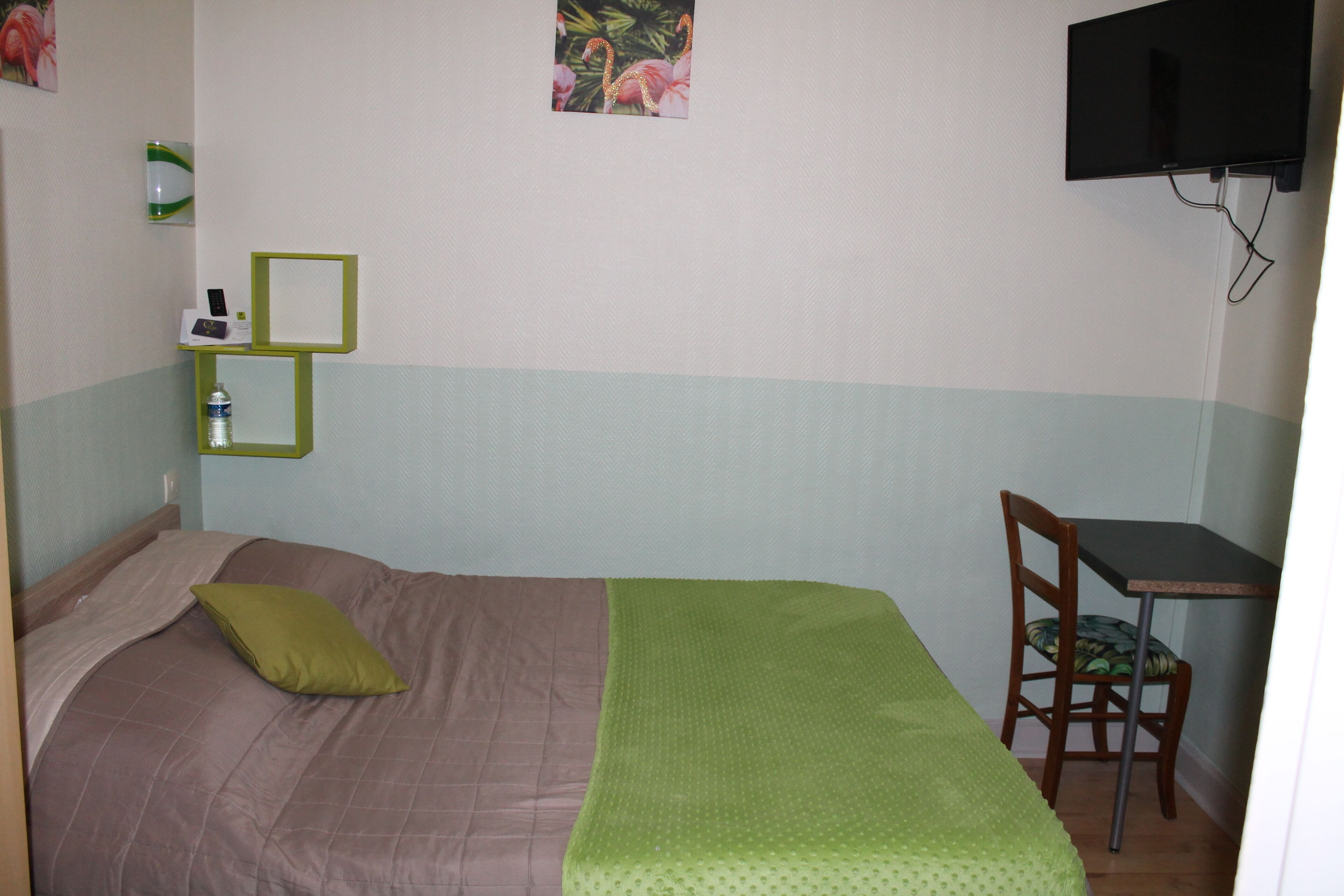 A small room with a bed, a desk, a chair, a TV, and a water bottle on a shelf.