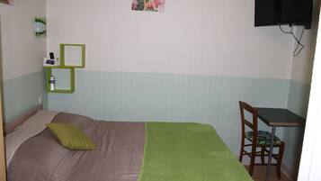 A small room with a bed, a desk, a chair, a TV, and a water bottle on a shelf.