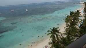 A beach with clear turquoise waters, palm trees, and a few boats. - Kristhal Plaza (San Andrés)