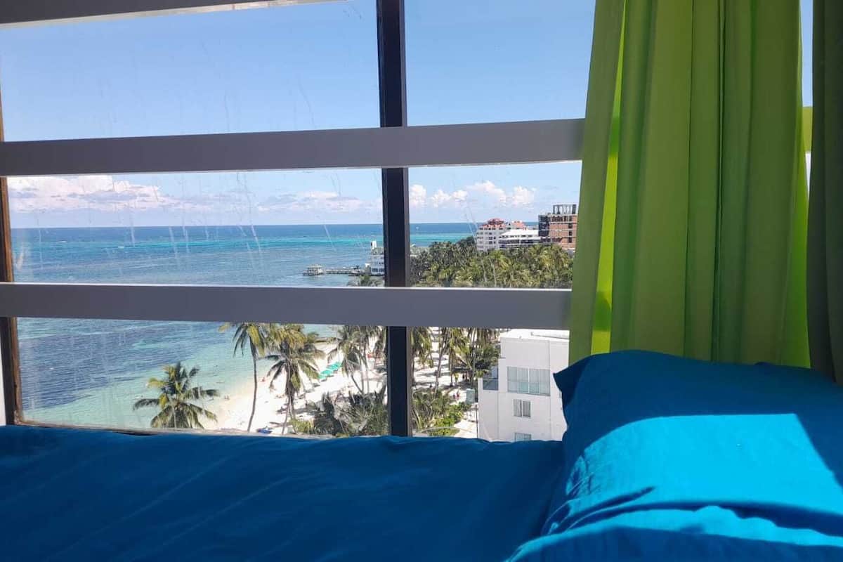 A room with a large window offering a view of the ocean and a beach.