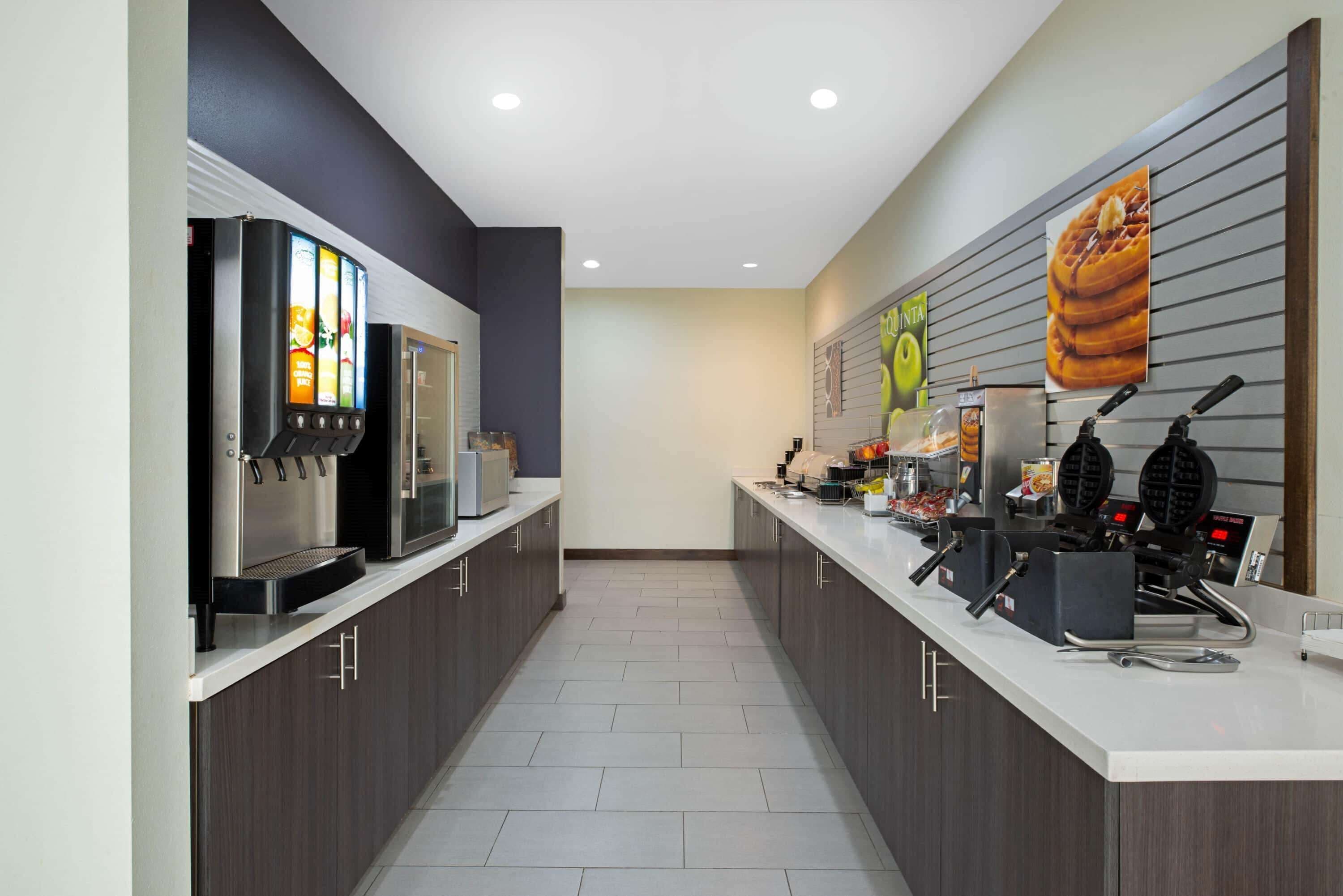 Un espace cuisine moderne équipé d’une machine à café, d’un appareil à gaufres et de divers produits alimentaires disposés sur le comptoir.