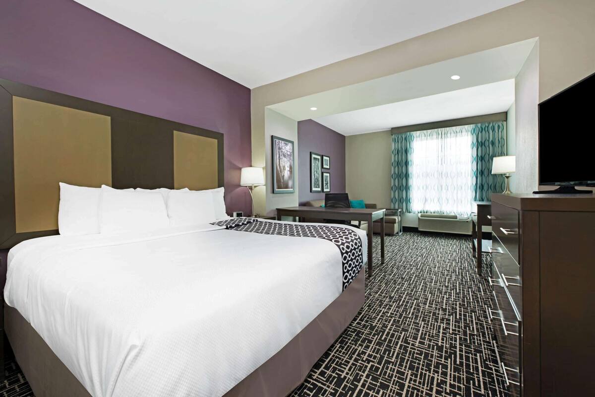 A hotel room with a large bed, a desk, a chair, a television, and a window with curtains.