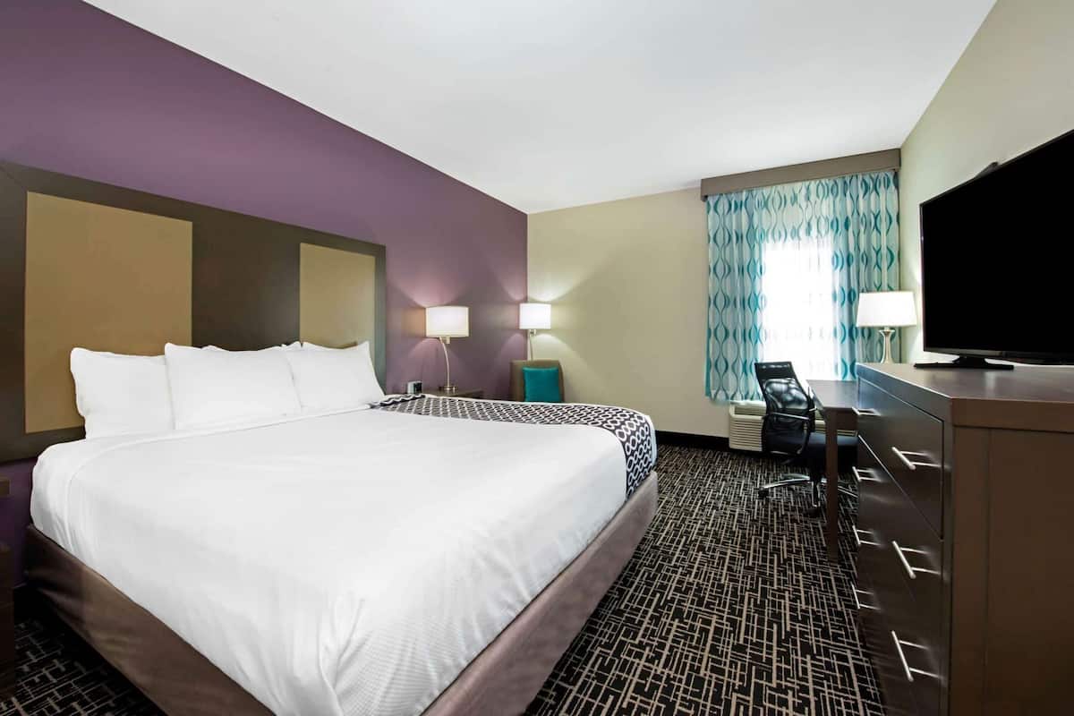 A hotel room with a large bed, two bedside lamps, a television, a desk with a chair, and a patterned carpet.