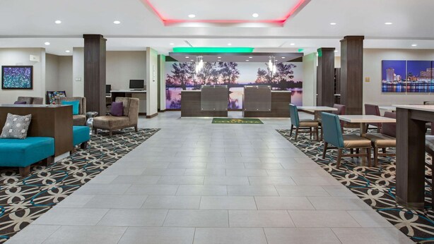 A hotel lobby with a reception desk, seating area, and a large window with a cityscape view. - La Quinta Inn & Suites by Wyndham Lake Charles - Westlake (Westlake)