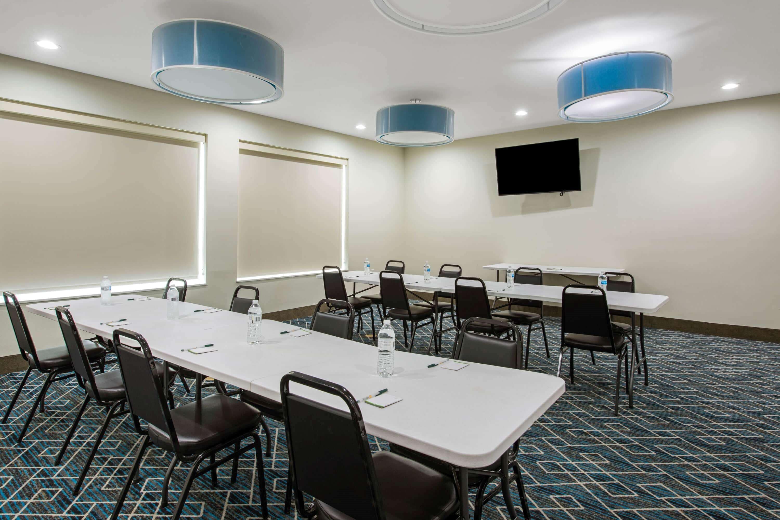 A conference room with a long table, chairs, a projector screen, and a flat-screen TV on the wall.