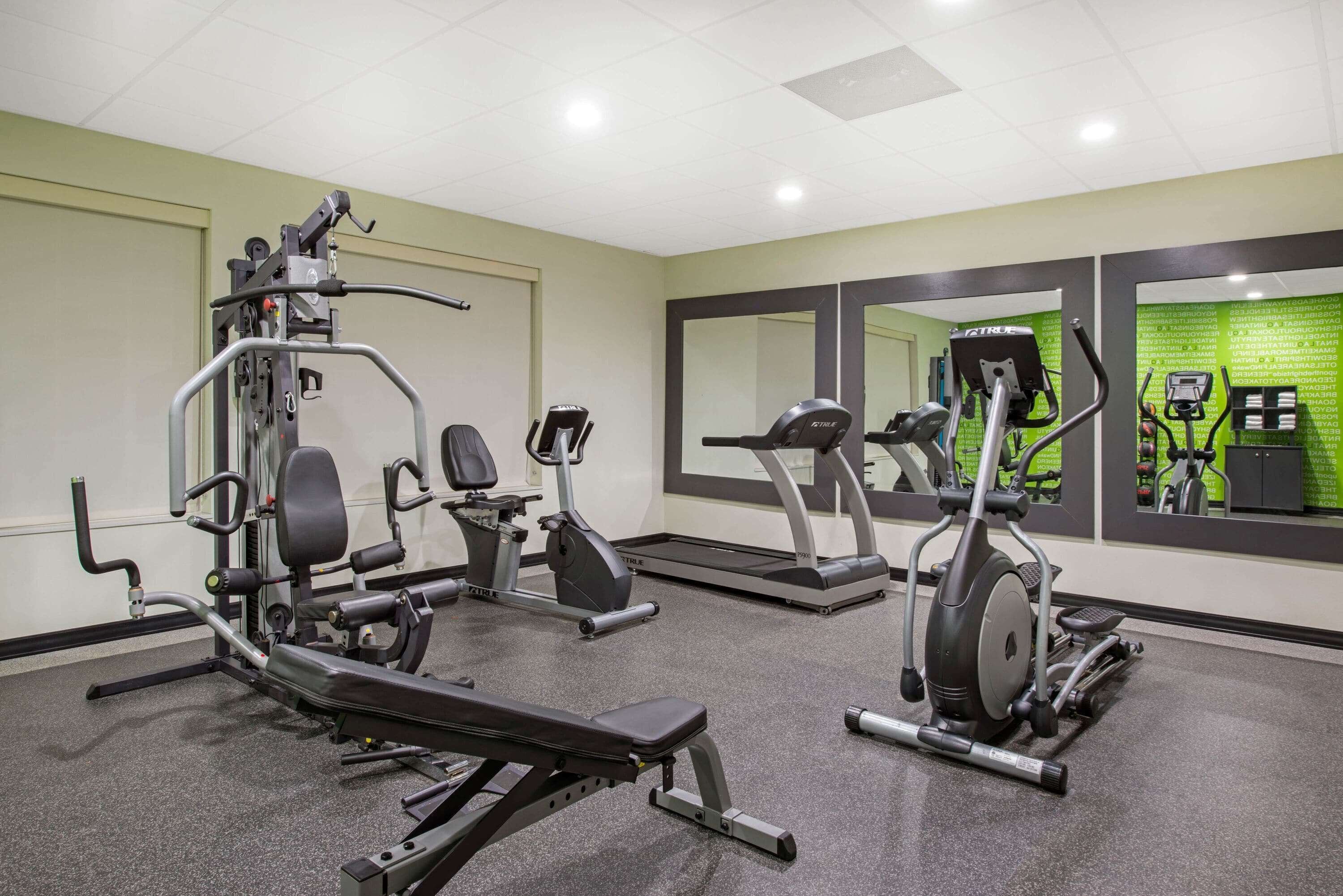 Ett gym med olika typer av träningsutrustning, inklusive en bänkpress, ett löpband och en crosstrainer.