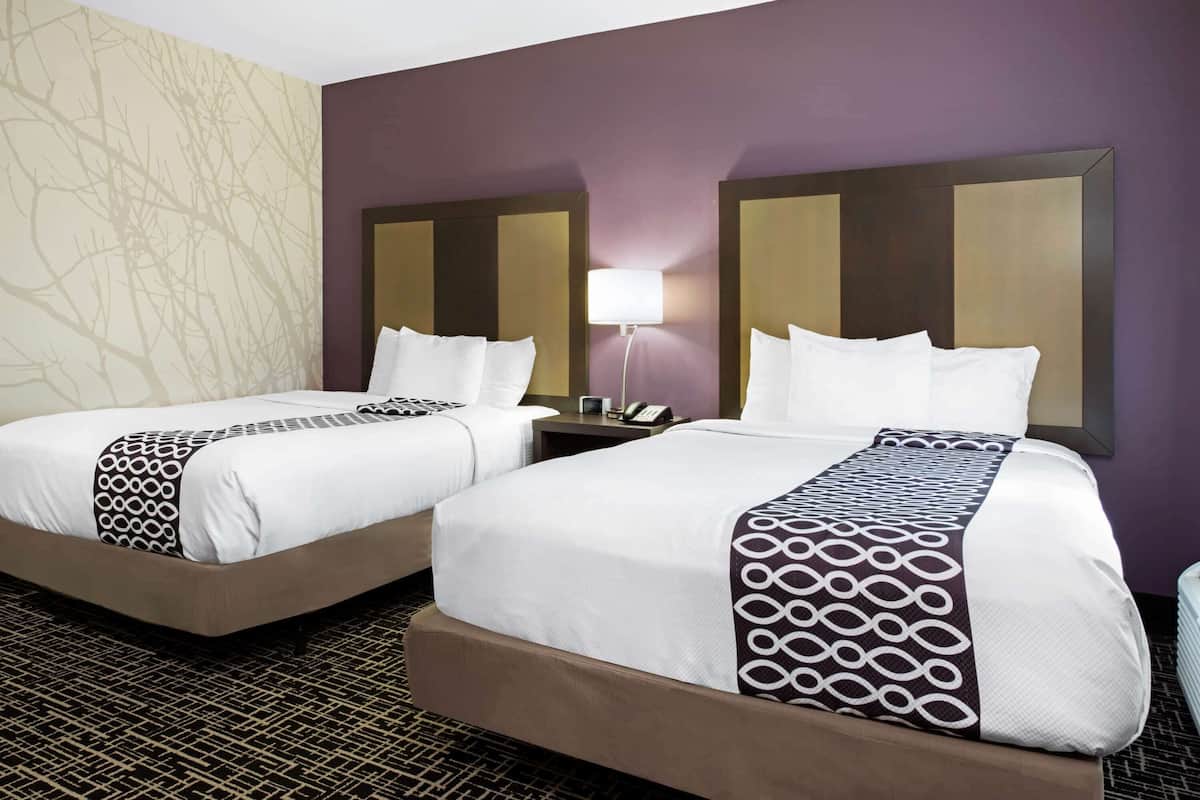 A hotel room with two beds, a patterned rug, and a wall with a tree branch design.