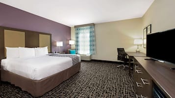 Habitación de hotel con una cama grande, un escritorio con televisor de pantalla plana, una silla, una lámpara de escritorio y una ventana con cortinas.