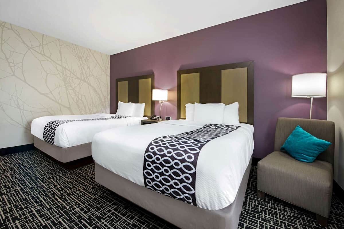 A hotel room with two beds, a sofa, a lamp, and a patterned carpet.