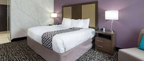 Una habitación de hotel con una cama grande, una mesita de noche con lámpara, un aparador y una silla.