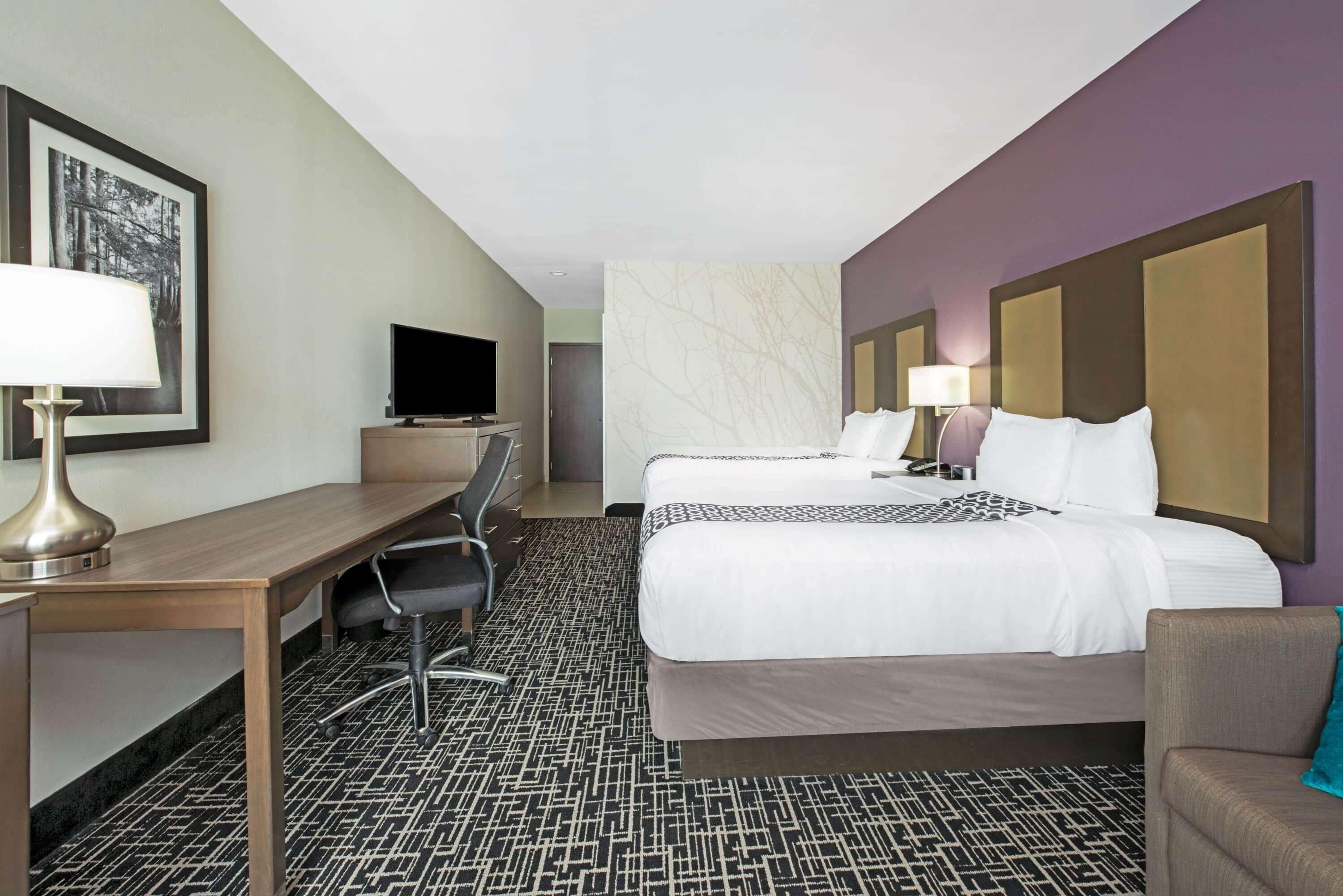 A hotel room with a bed, a desk, a chair, a television, and a lamp.