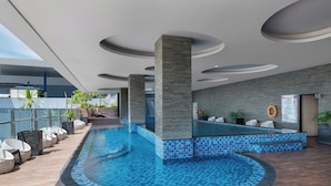A modern indoor swimming pool with a tiled edge, surrounded by lounge chairs and a stone wall. - Melia Makassar (Makassar)