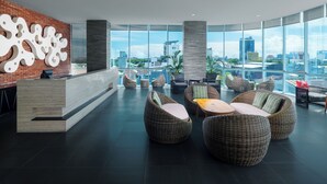 A modern lobby with a reception desk, wicker seating, and large windows offering a city view. - Melia Makassar (Makassar)