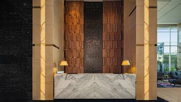 A reception area with a marble counter, wooden panel wall, and two lamps.