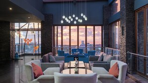 A modern lounge with comfortable seating, a central table, and large windows offering a city view. - Melia Makassar (Makassar)