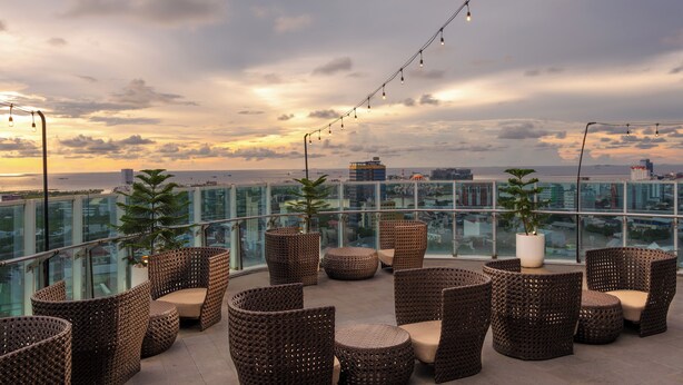 A rooftop terrace with wicker furniture, string lights, and potted plants. - Melia Makassar (Makassar)