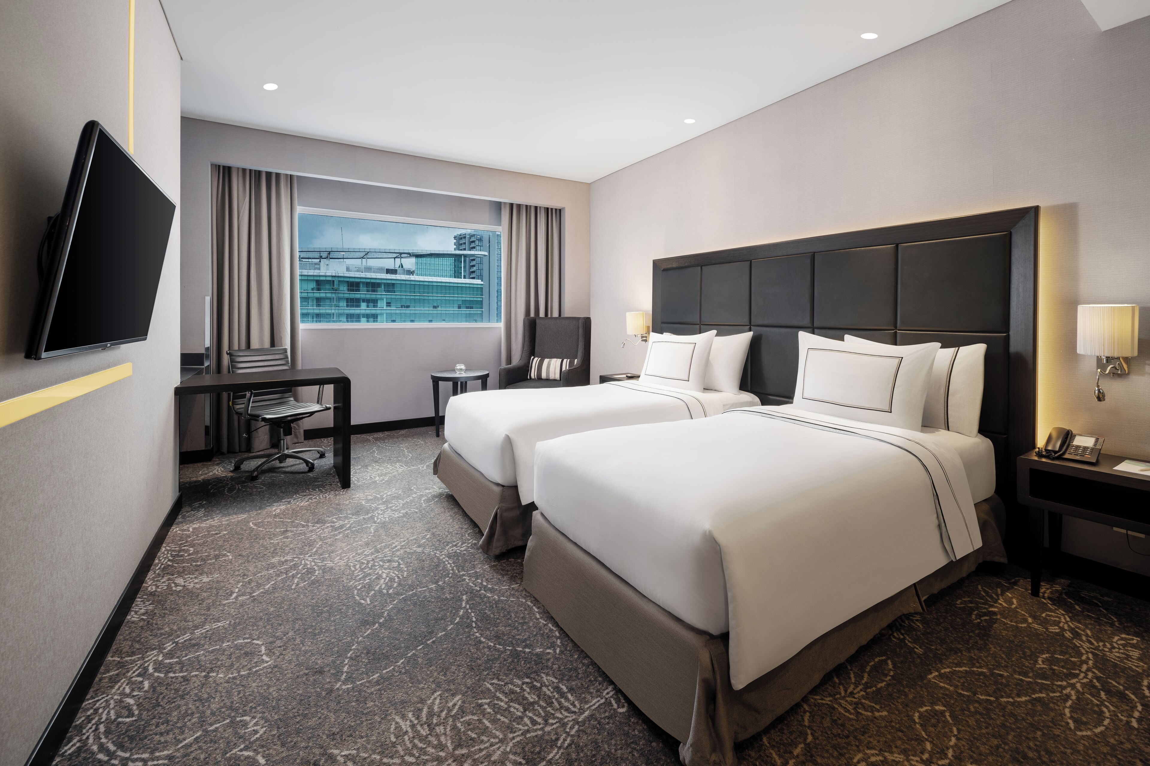 Habitación de hotel con dos camas, un escritorio, una silla, un televisor y vista a la ciudad.