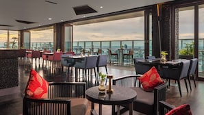 A spacious indoor area with multiple tables and chairs, large windows offering a city view, and a modern ceiling design. - Melia Makassar (Makassar)