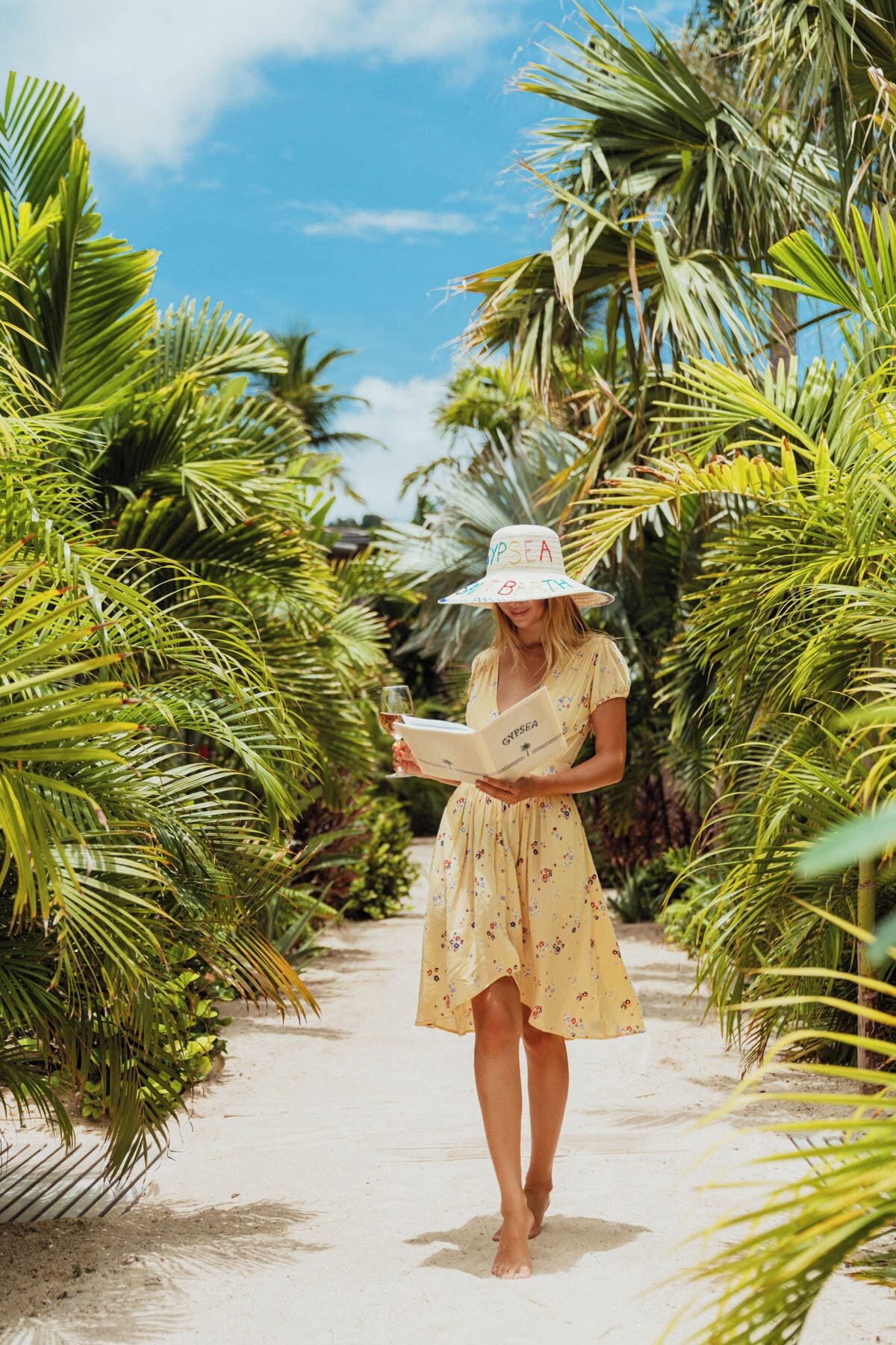 A person walking on a sandy path surrounded by palm trees, holding a book titled "GYPSSEA".