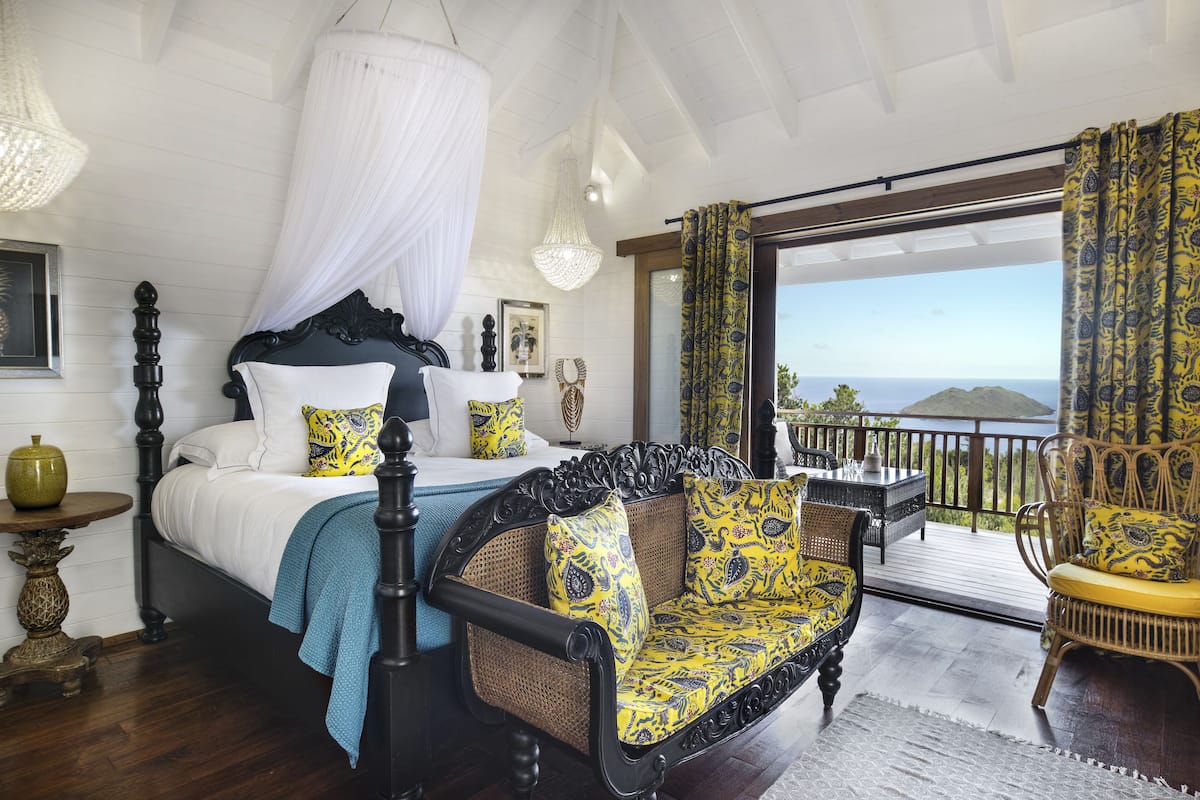 Un dormitorio con cama con dosel, un balcón con muebles de mimbre y vista al océano.