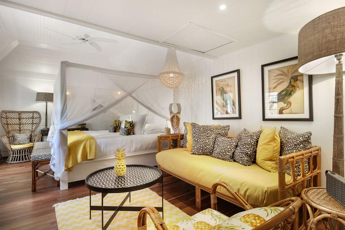 Una habitación con cama, sofá, muebles de mimbre, una mesa redonda y obras de arte en las paredes.