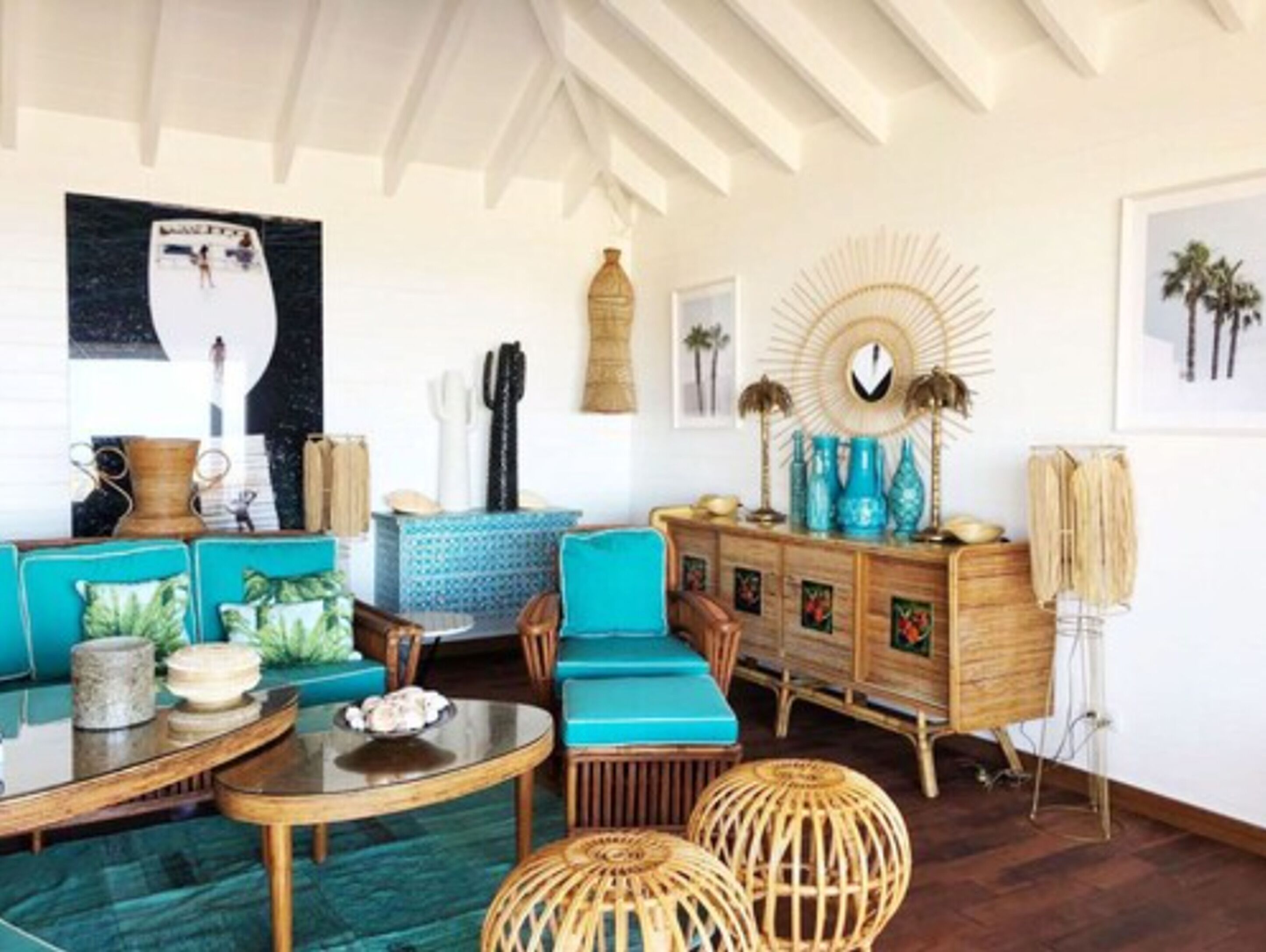 Une pièce comprenant une table ronde en verre, des chaises recouvertes d’un tissu turquoise, un meuble en bois orné d’objets décoratifs et un grand miroir mural.