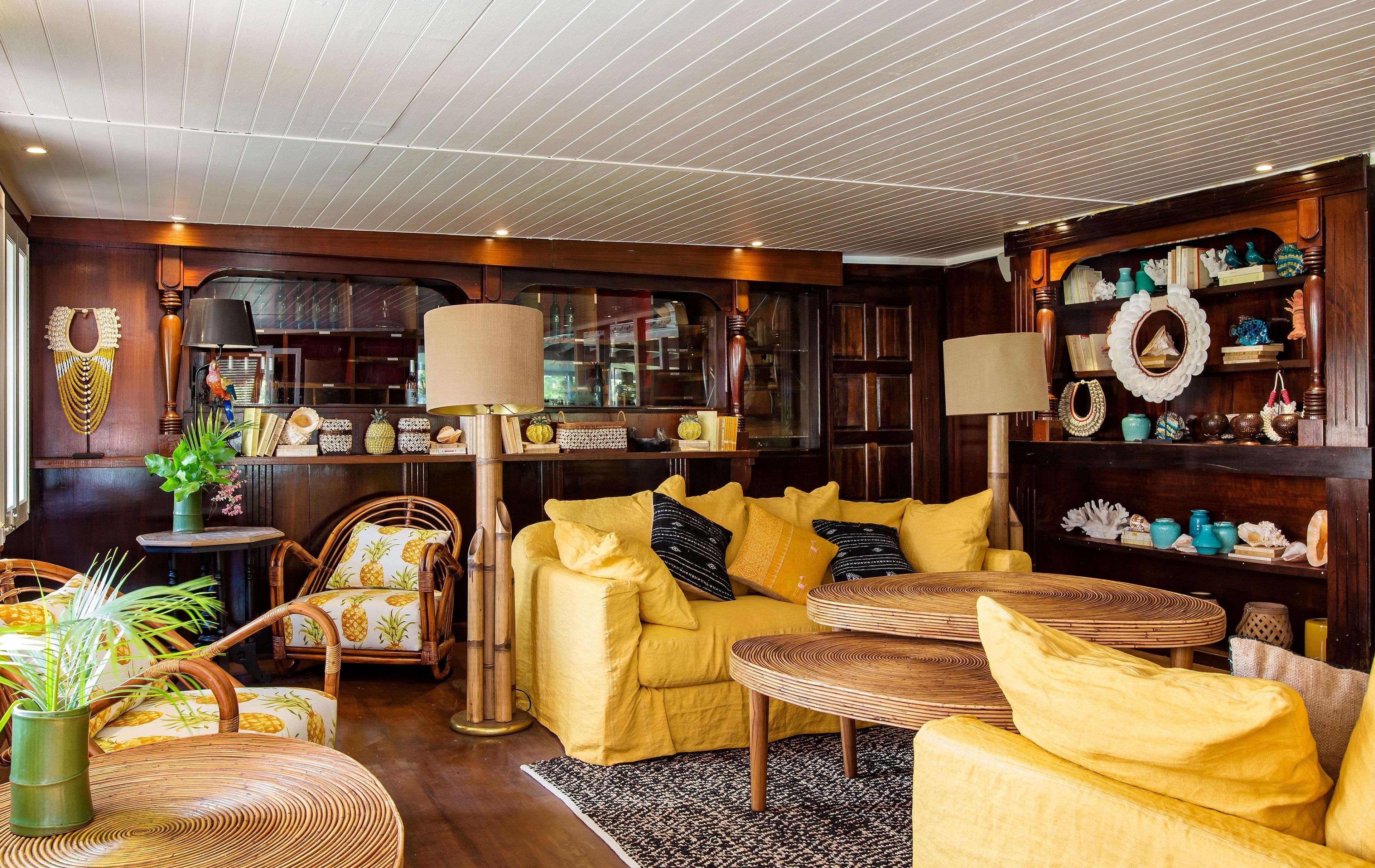 Una sala de estar acogedora con un sofá amarillo, sillas de mimbre, una mesa redonda y una estantería llena de objetos decorativos.