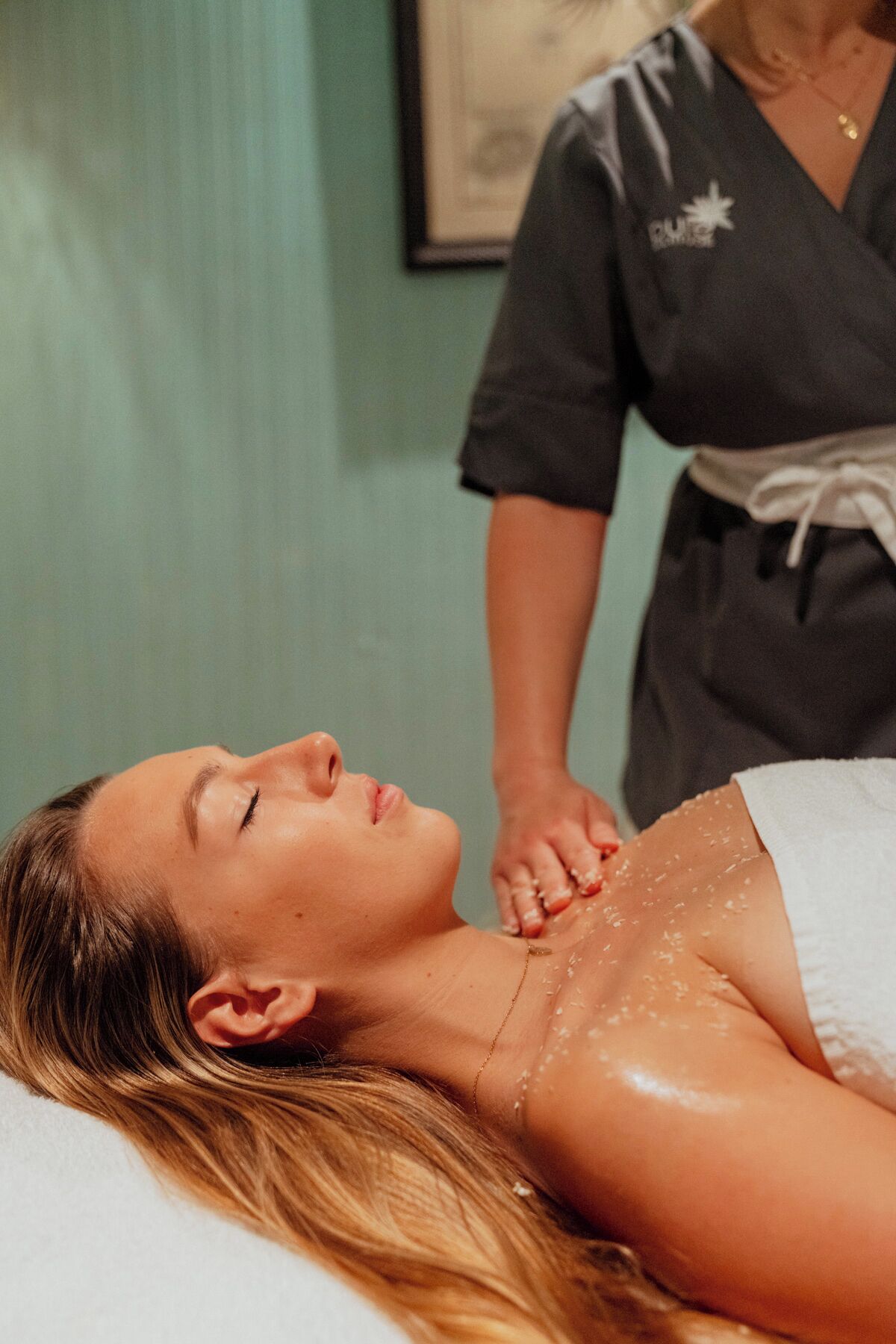 A person lying on a bed with a white sheet, receiving a massage.