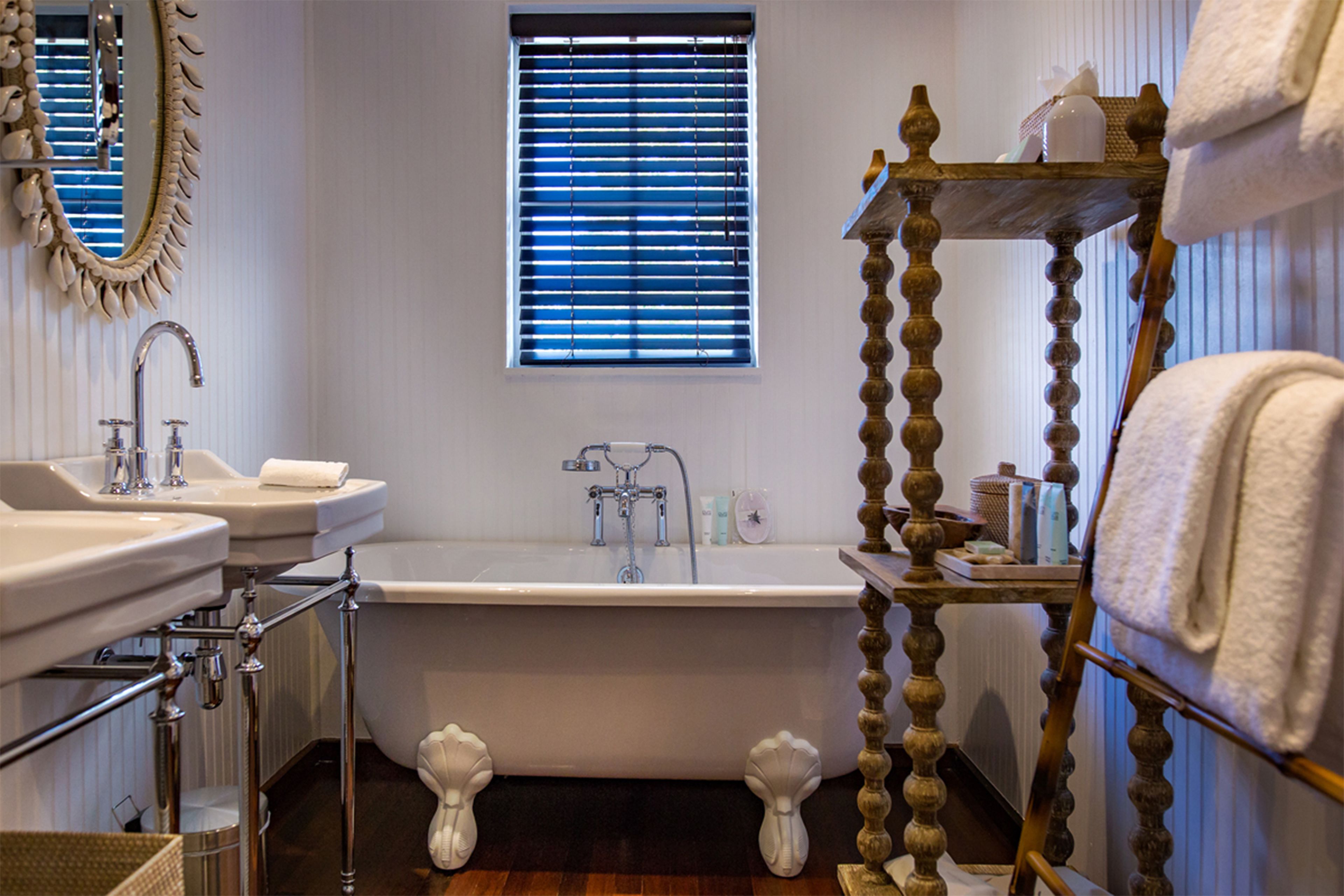 A bathroom with a bathtub, two sinks, a vanity, and a wooden shelf with towels.