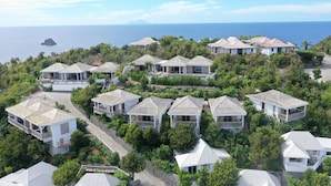 Una zona residencial costera con varias casas, algunas con balcones, rodeada de exuberante vegetación y vista al mar.