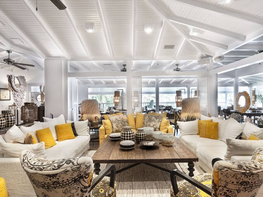 A spacious living area with white sofas and yellow cushions, a wooden coffee table, and decorative vases.