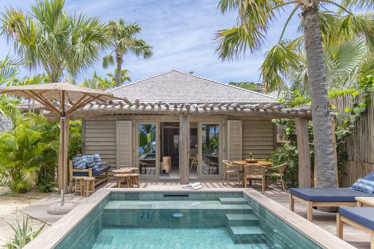 Zona junto a la piscina con un espacio de descanso cubierto, una piscina y plantas tropicales.