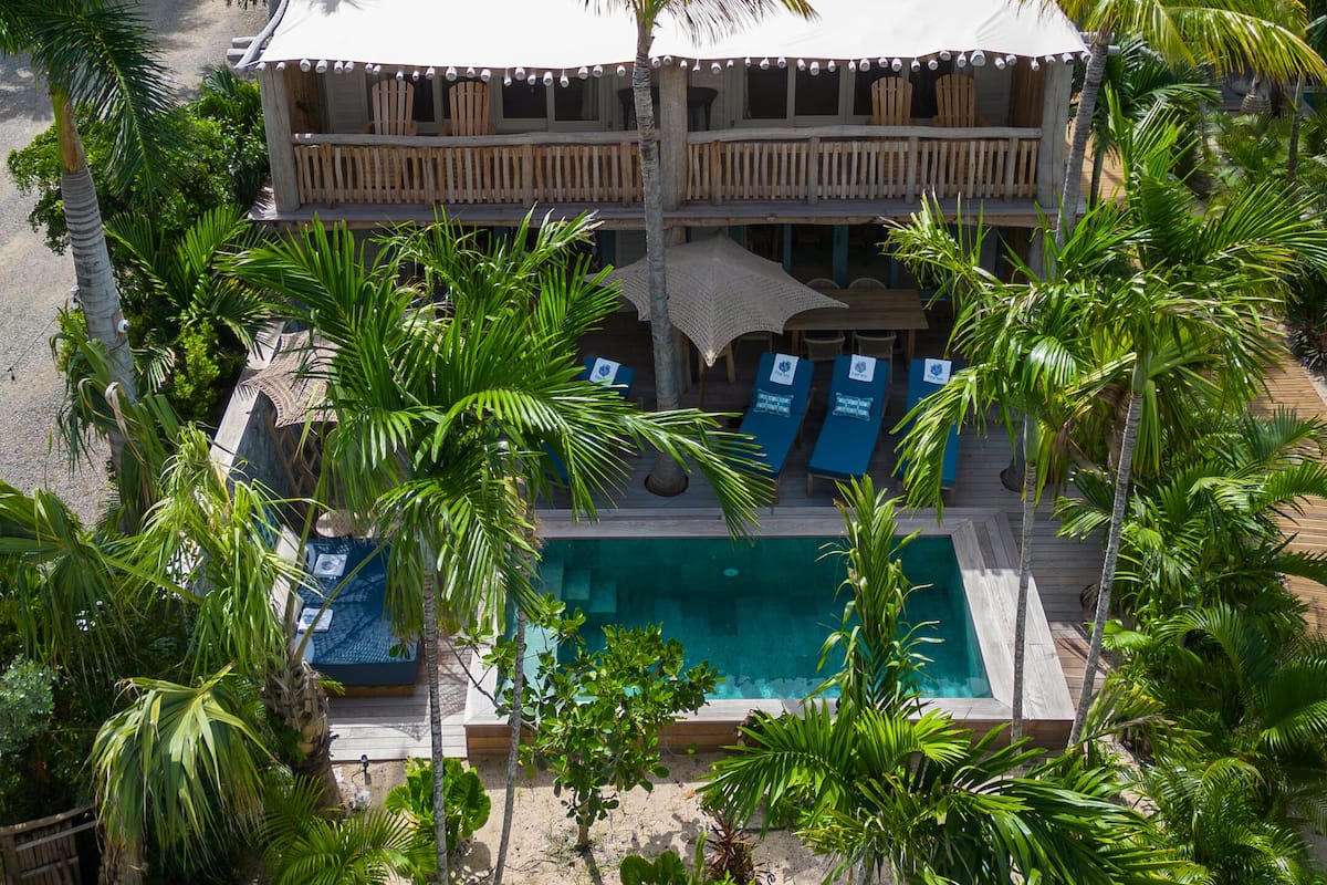 Un resort con piscina, rodeado de palmeras y vistas a una colina con casas.