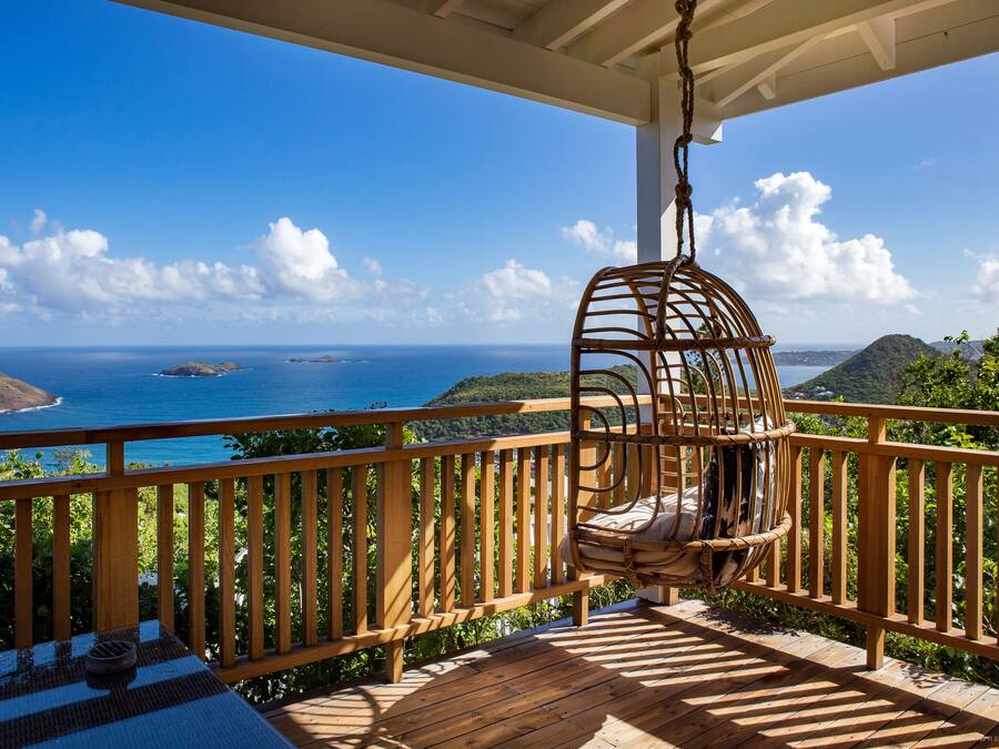 Terraza de madera con una silla colgante con vistas a la costa.