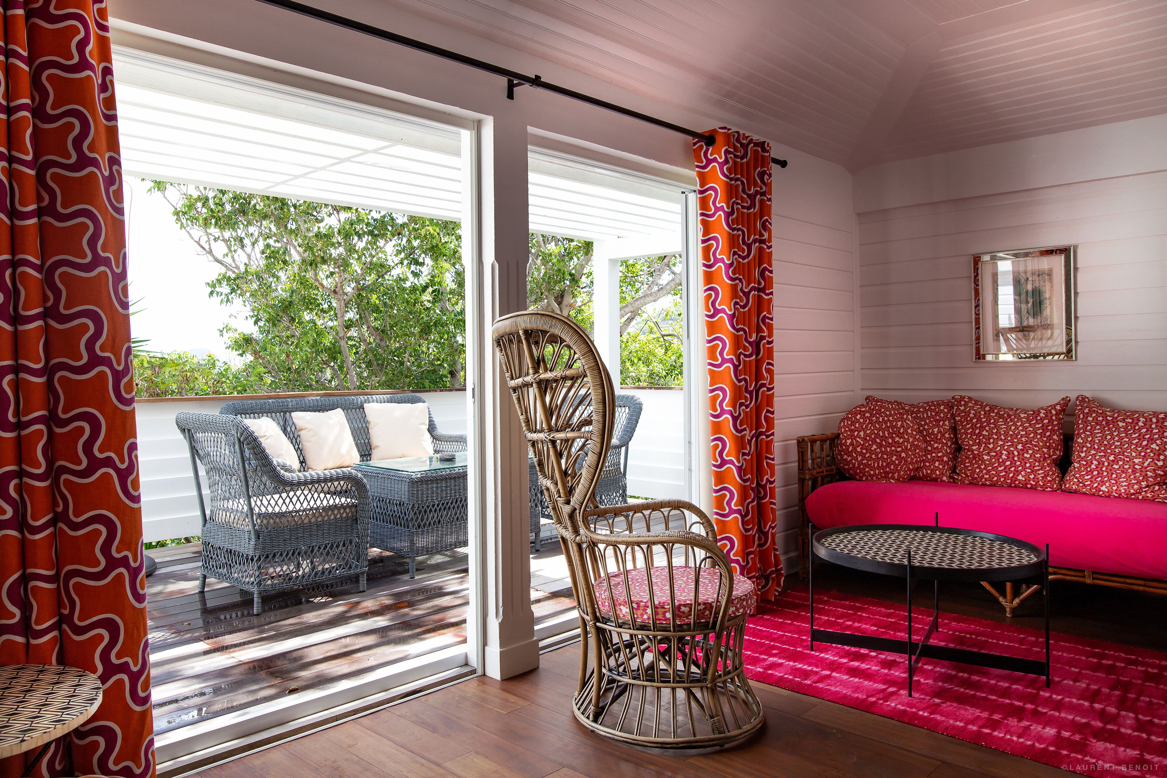 A room with a wicker chair, a round table, and a sofa with patterned cushions.