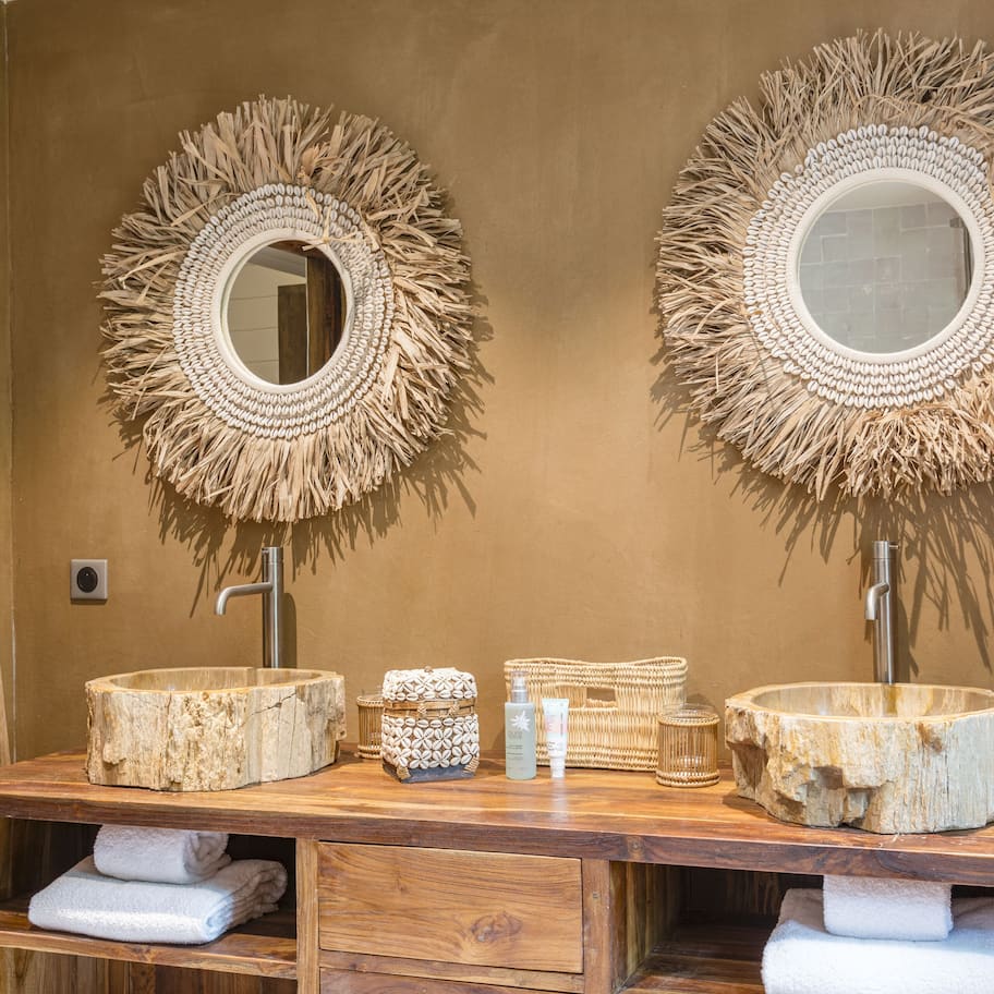 A bathroom with two large woven mirrors, a wooden vanity, and a ladder.