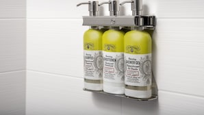 Casa de banho com três produtos J.R. Watkins: champô, condicionador e gel de banho, montados num dispensador fixado na parede.